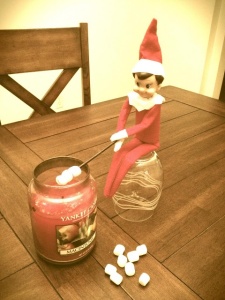 Elf on the Shelf roasting some marshmallows over a candle flame